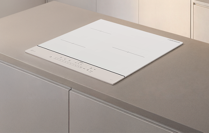 미니멀한 주방 조리대 위에 흰색의 평면 인덕션이 놓여 있다. 베이지 톤 상판과 밝은 벽면이 어우러져 깔끔하고 정돈된 분위기를 만든다.